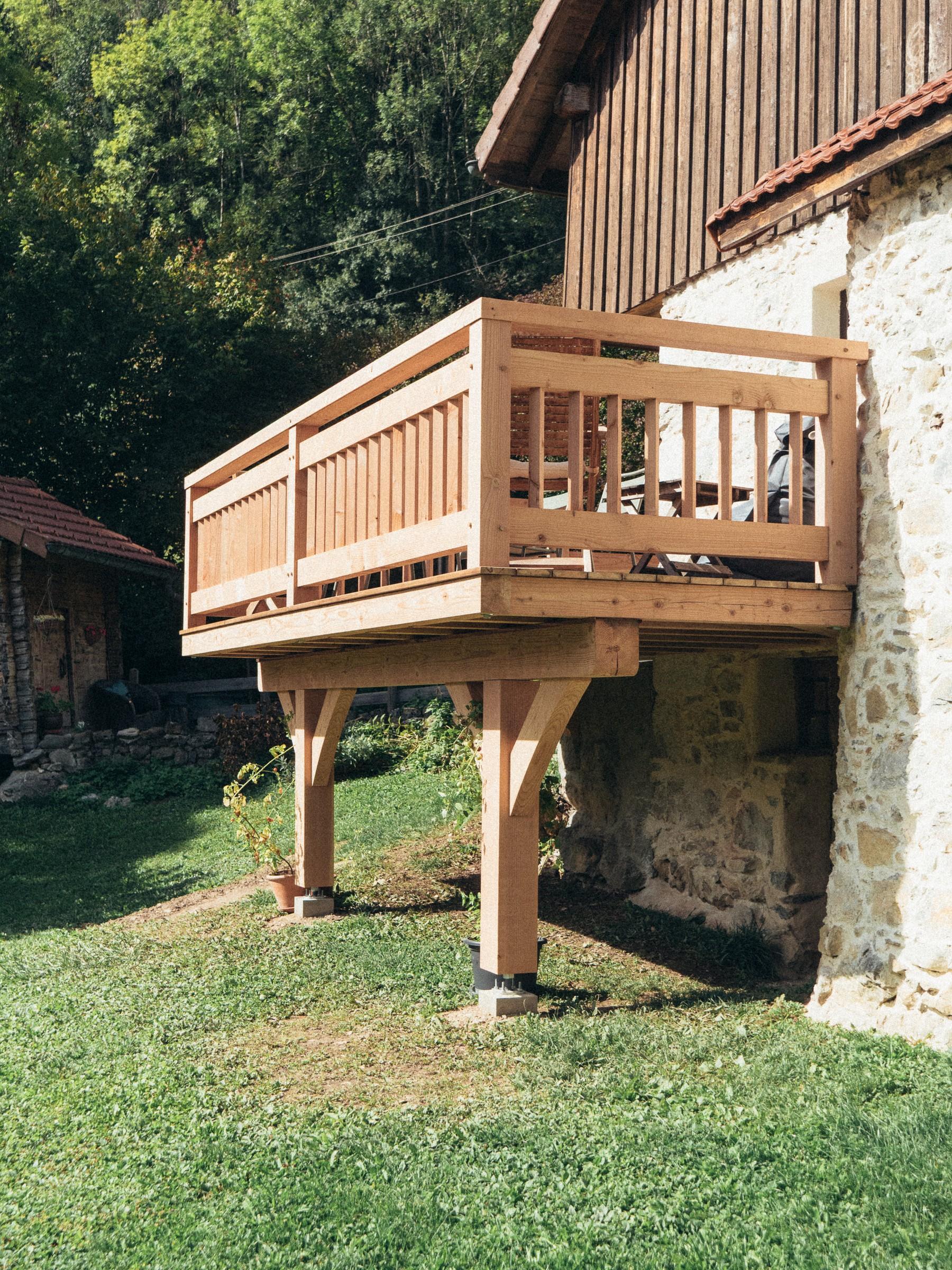 Balcon en bois sur poteaux, adossé à un mur en pierre, réalisé par Aravis Menuiserie